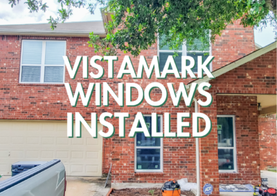 A newly installed window on a brick house with tools and equipment visible in the front yard.